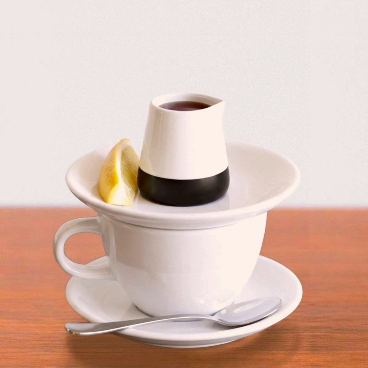 Lemon, honey and ginger brew in a small jug on a saucer over a white cup, with a lemon wedge