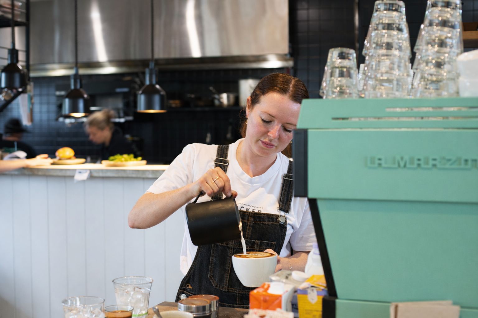 Latte art being poured beside the green Tucker machine