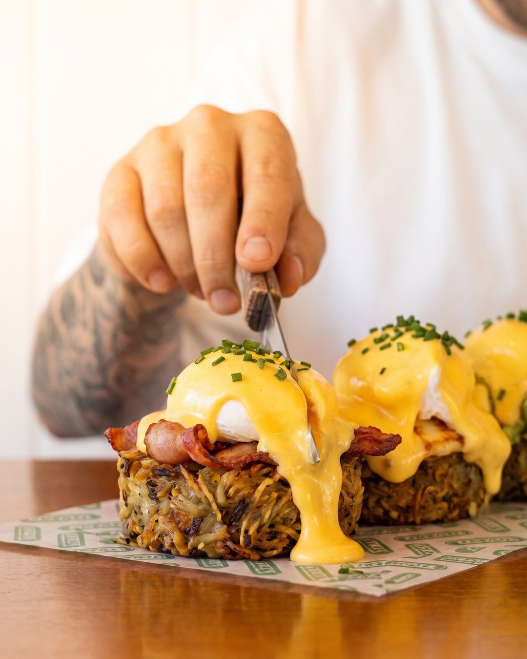 A knife cutting into a bacon rosti benedict with hollandaise