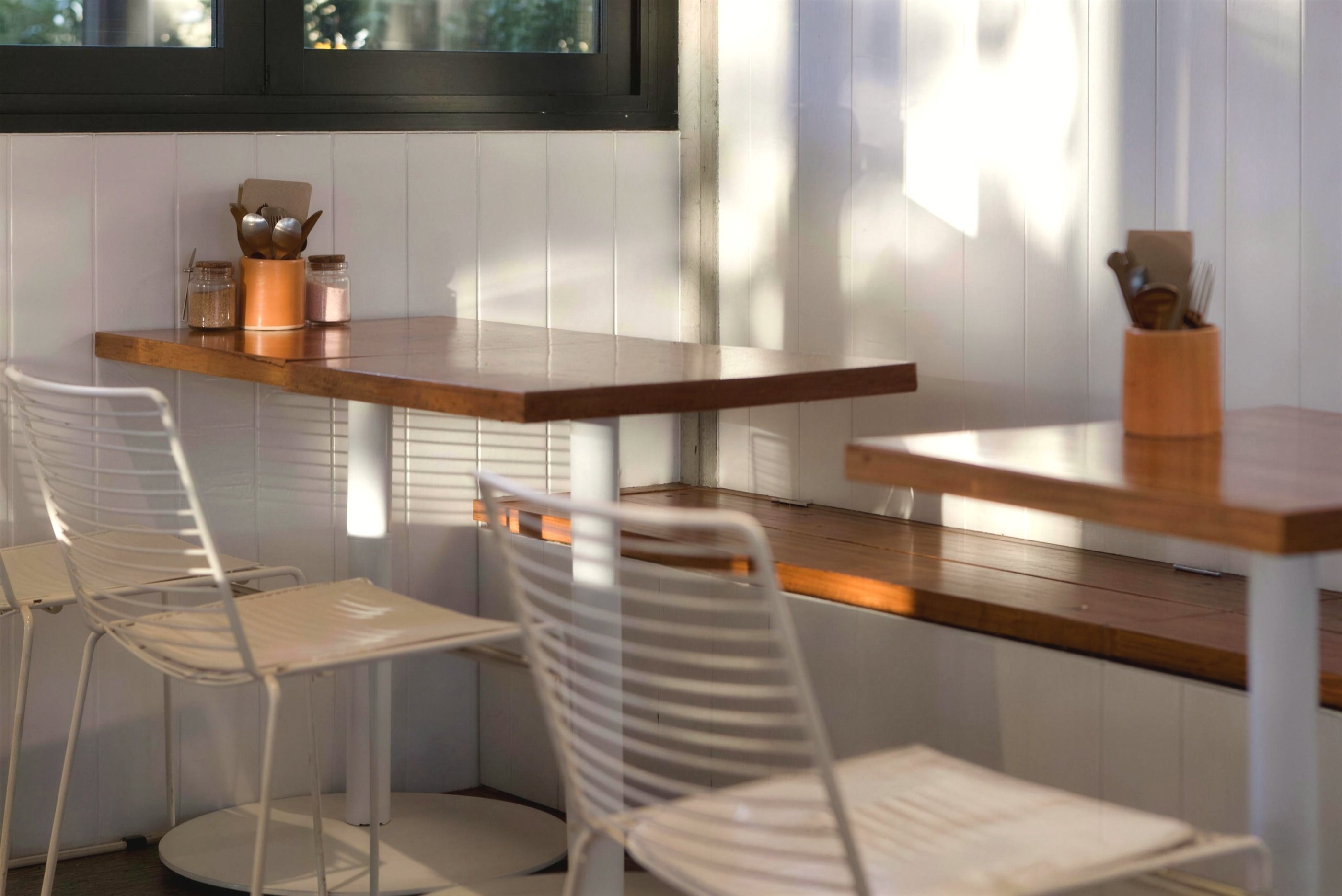 Window tables and white wire chairs in afternoon light at Tucker